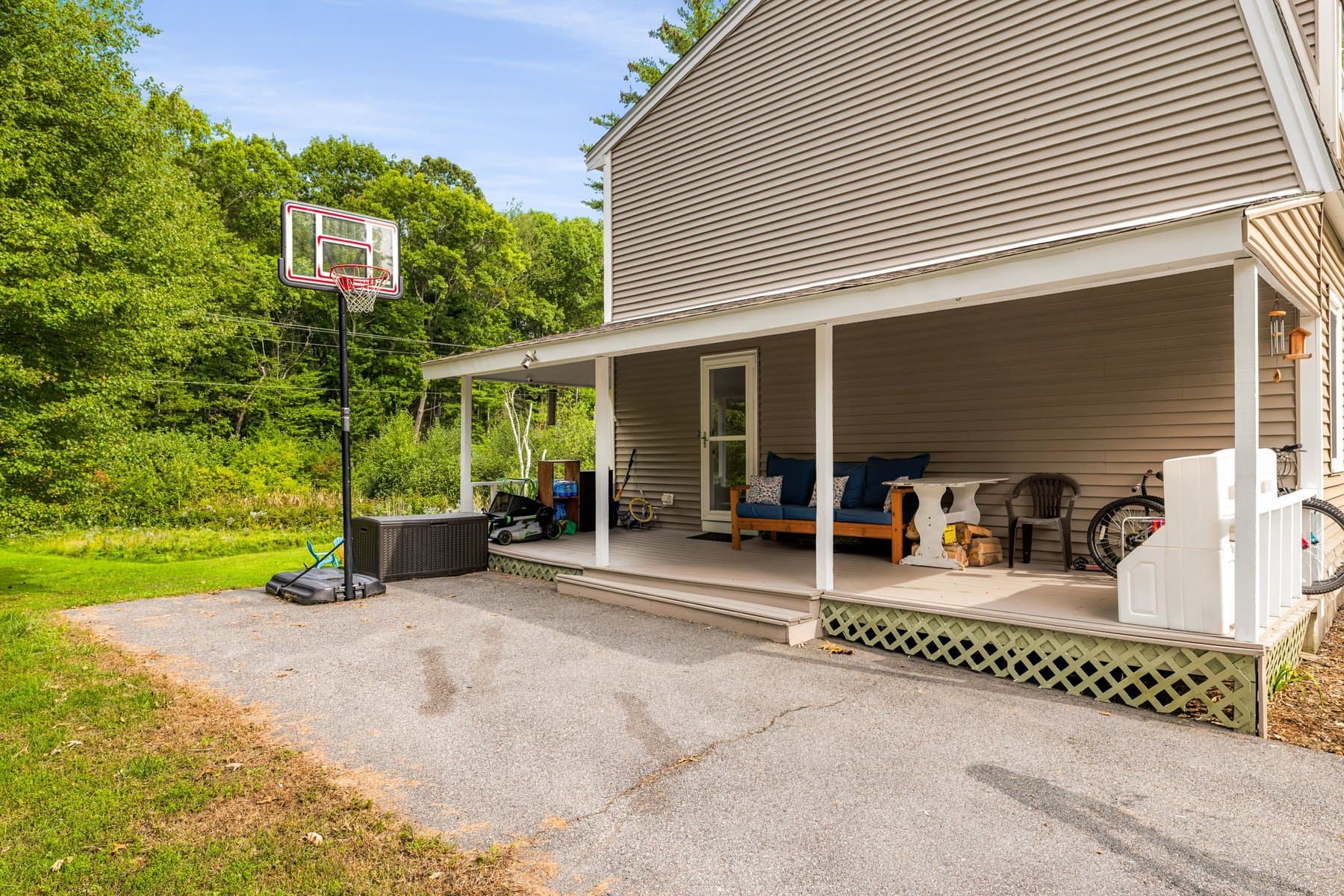 The covered porch along the end of the house, with an outdoor sofa and a basketball hoop on the driveway