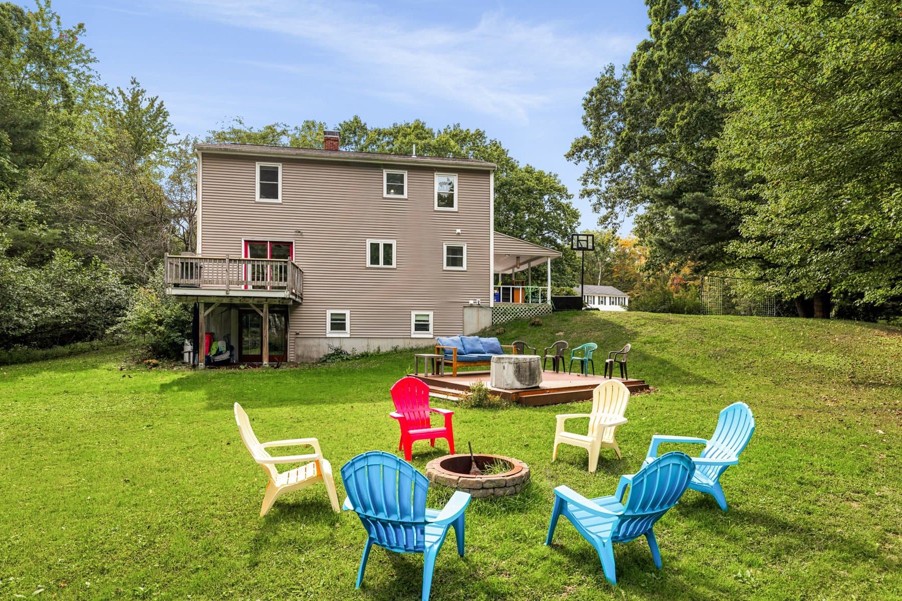 Adirondack chairs around the stone fire pit in the back lawn, with the house and the deck behind