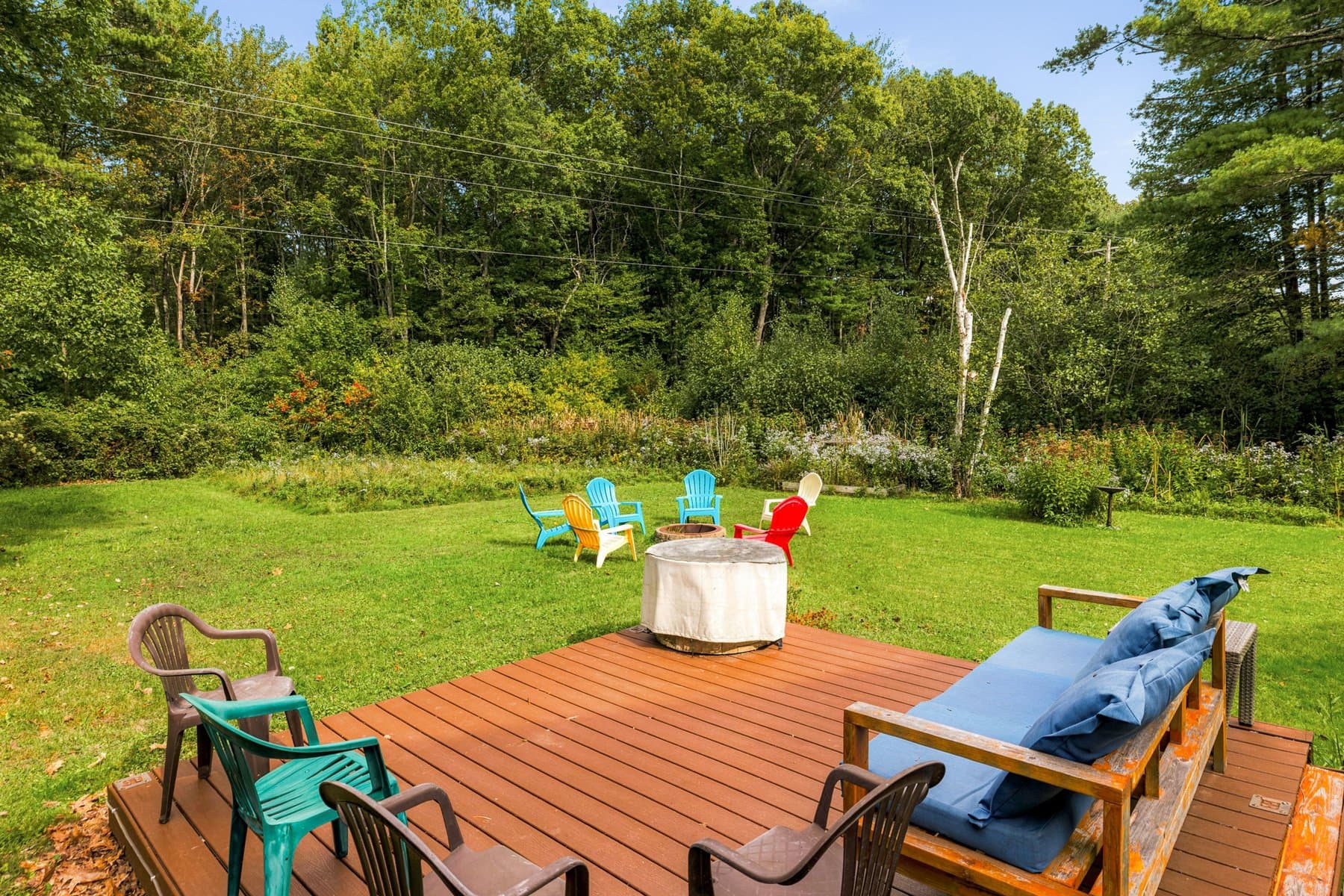 The freestanding deck at the edge of the woods, with an outdoor sofa and the fire pit beyond