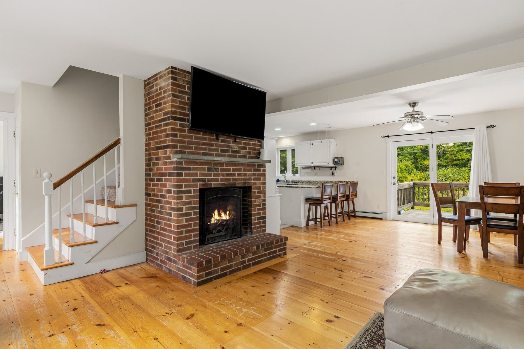 The living room with the brick fireplace lit, the stairs beside it, and the dining area and kitchen beyond