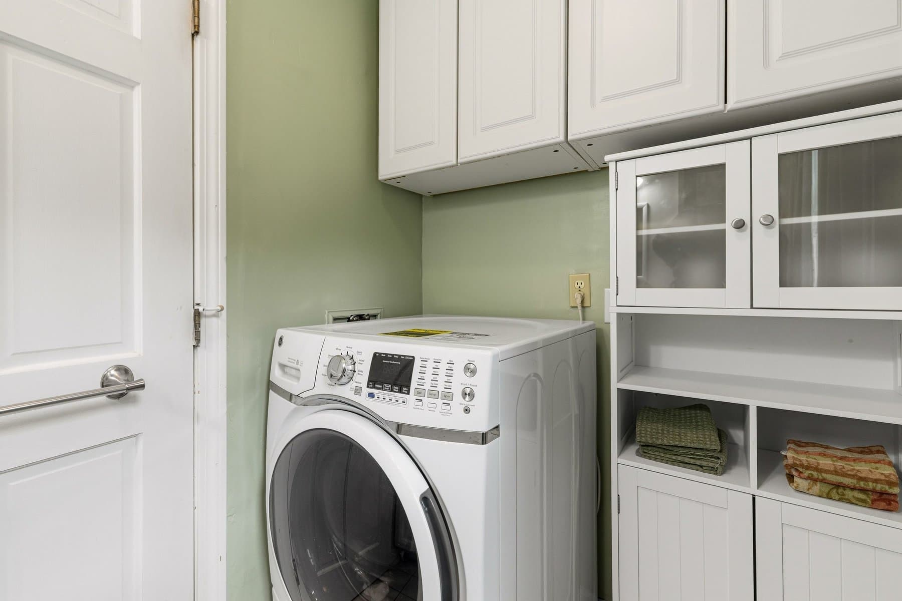 The laundry with a front-load washer and white cabinets, beside the half bath