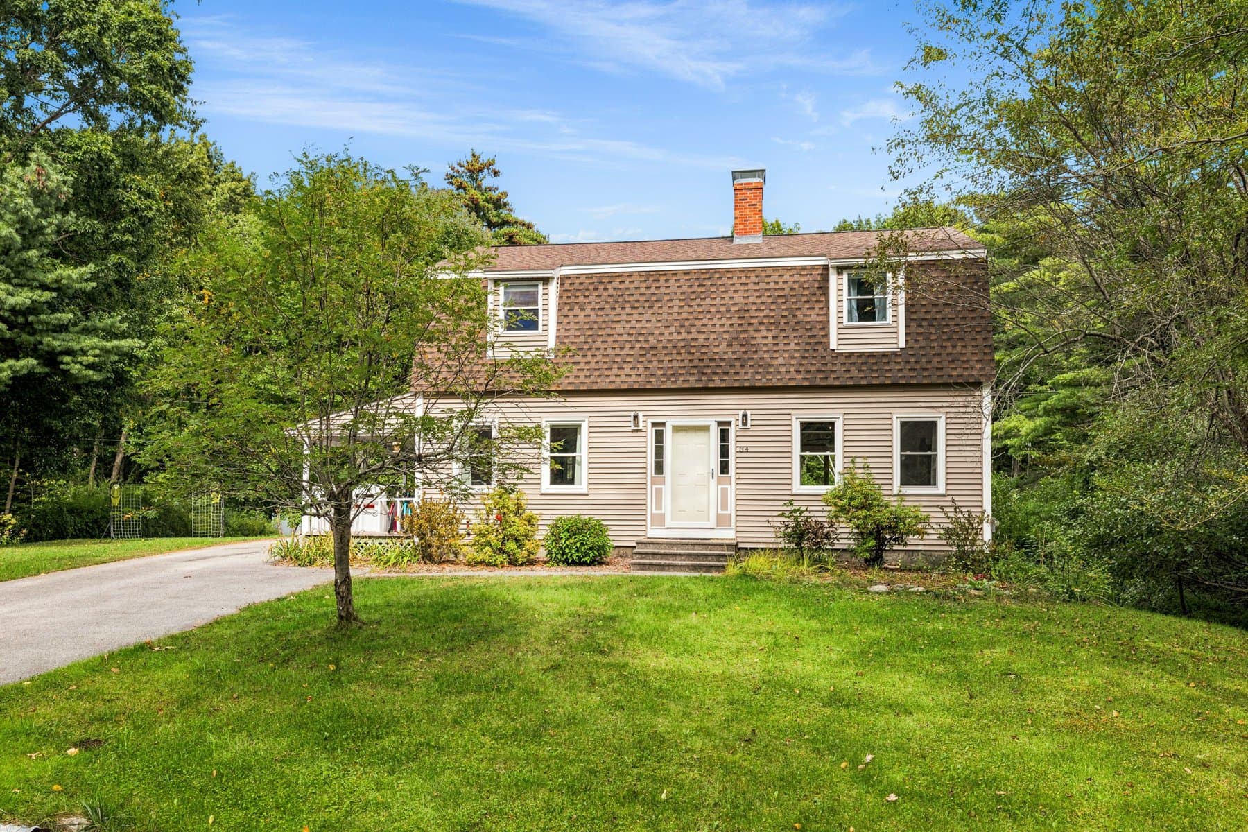 The gambrel from the front lawn, with the new siding, the brick chimney, and the woods behind